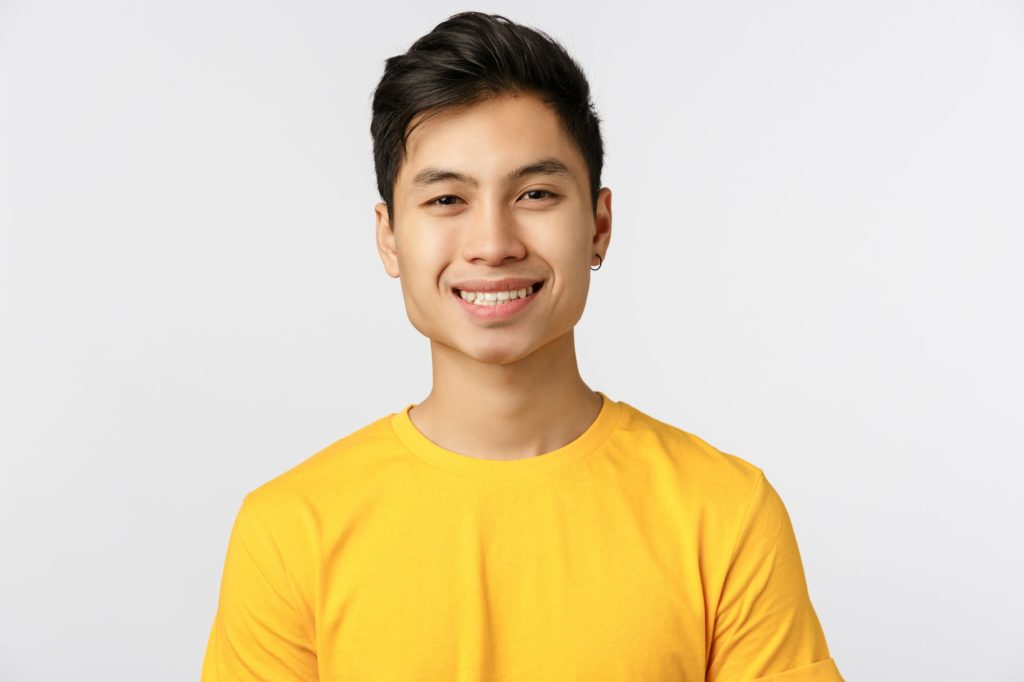 Close-up cheerful enthusiastic asian man with pierced ear, wear yellow t-shirt, smiling beaming grin